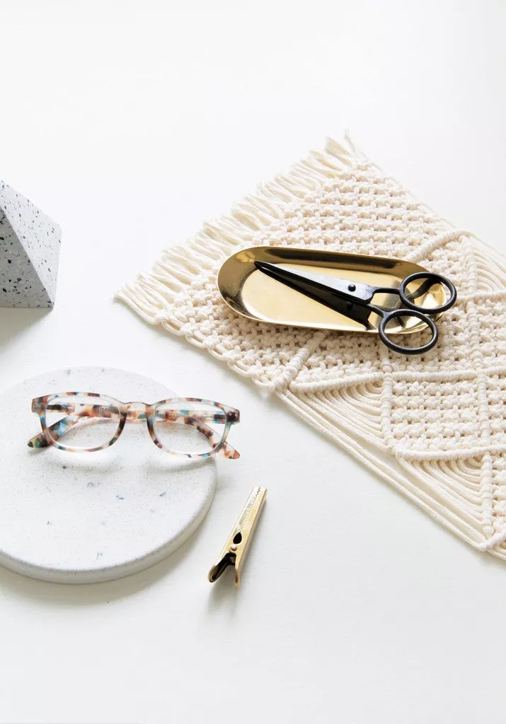 A macrame laptop mat with scissors and reading glasses